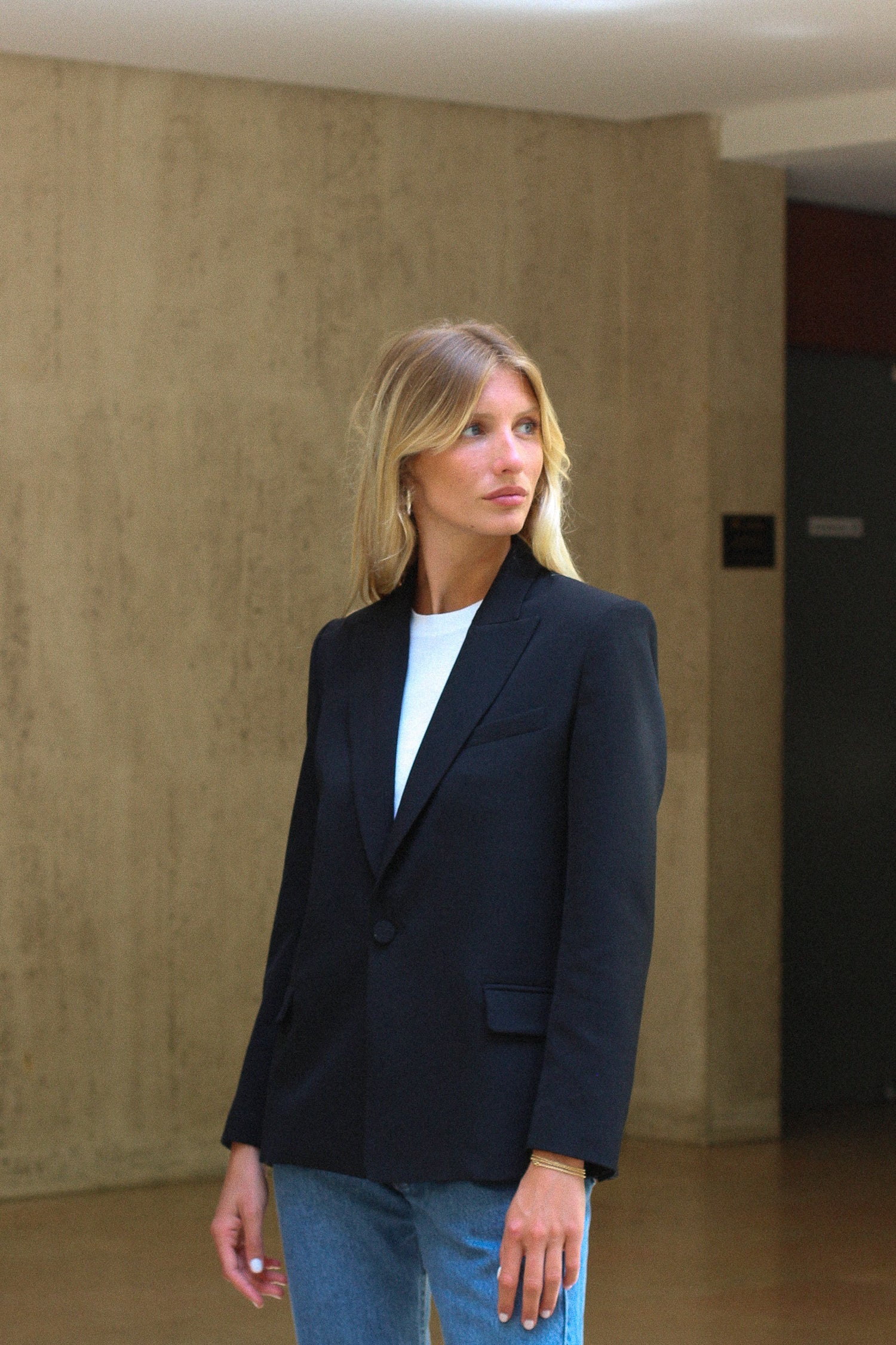 A model wearing the lauren black wool gabardine blazer in an aesthetically background. 100% made from sustainable upcycled wool. 