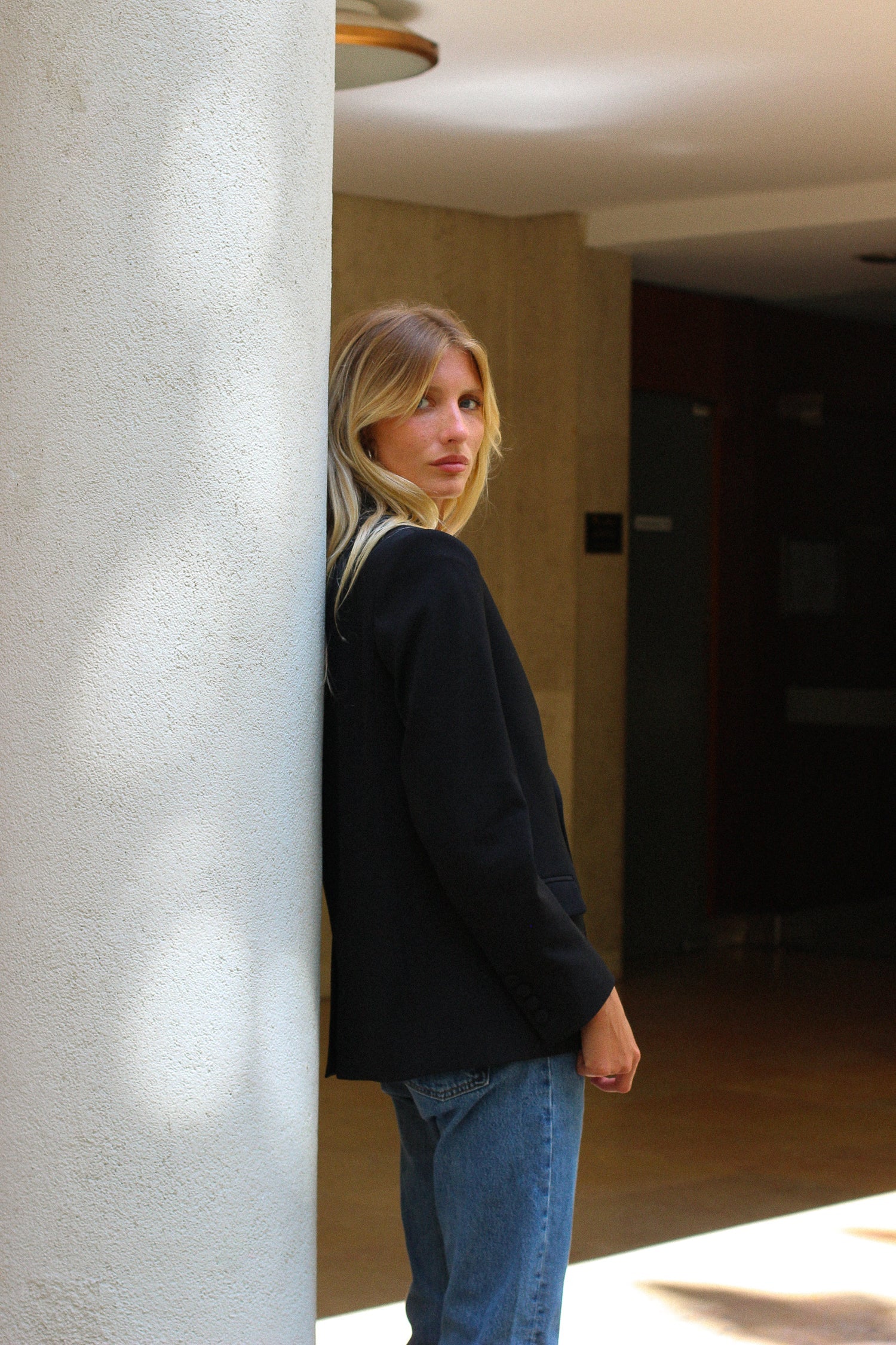 A model wearing the lauren black wool gabardine blazer in an aesthetically background. 100% made from sustainable upcycled wool. 