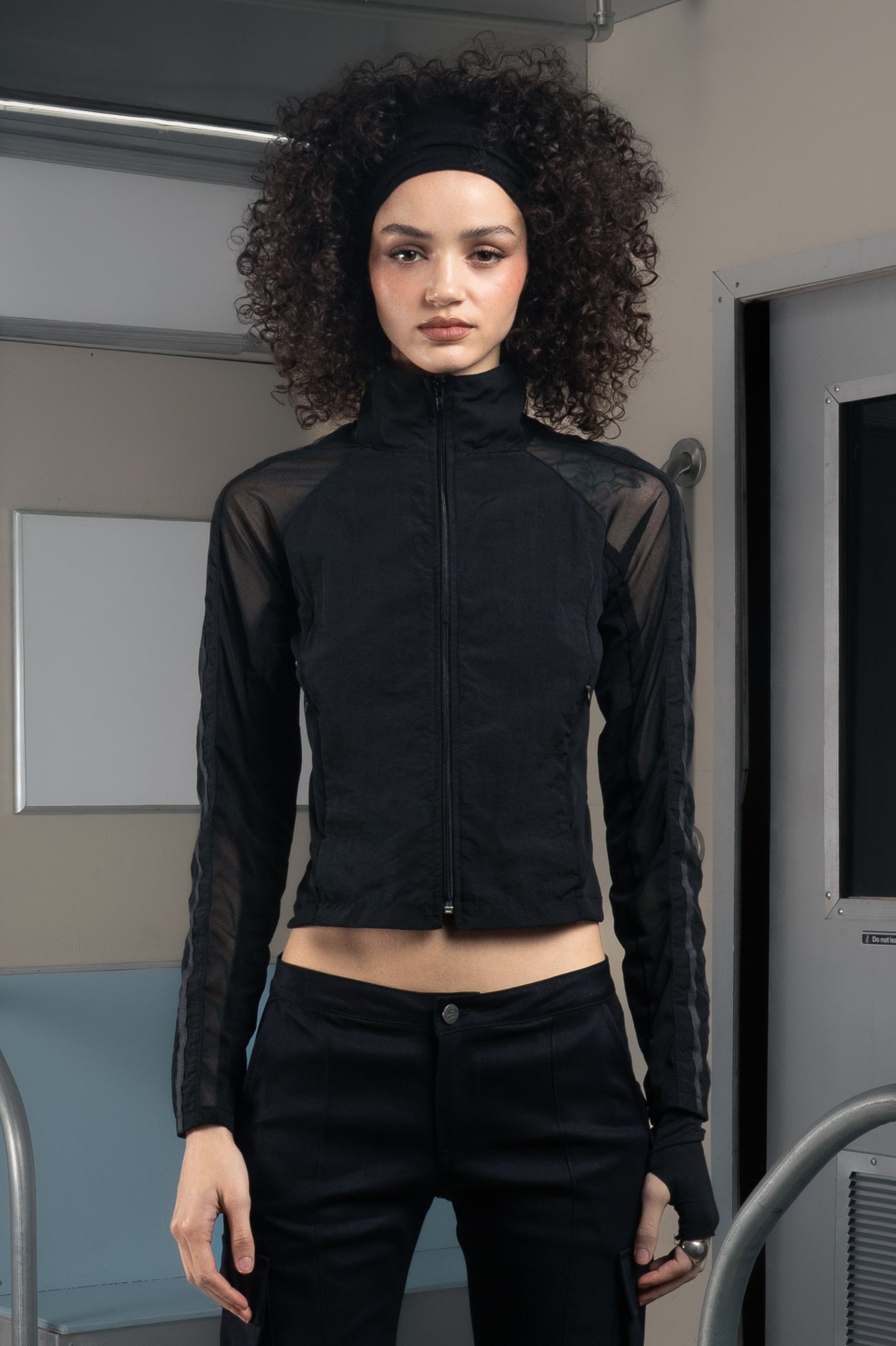 Woman wearing a black sheer sustainable jacket with deadstock pants in an indoor setting.
