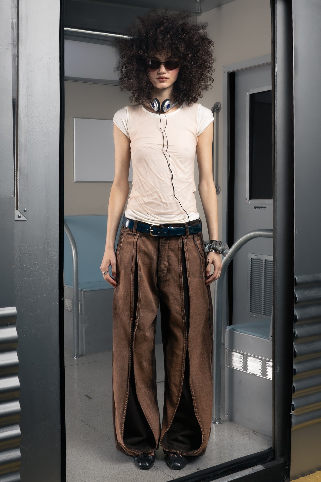 Woman wearing a sustainable light pink top and brown wide-leg pants in a futuristic subway.