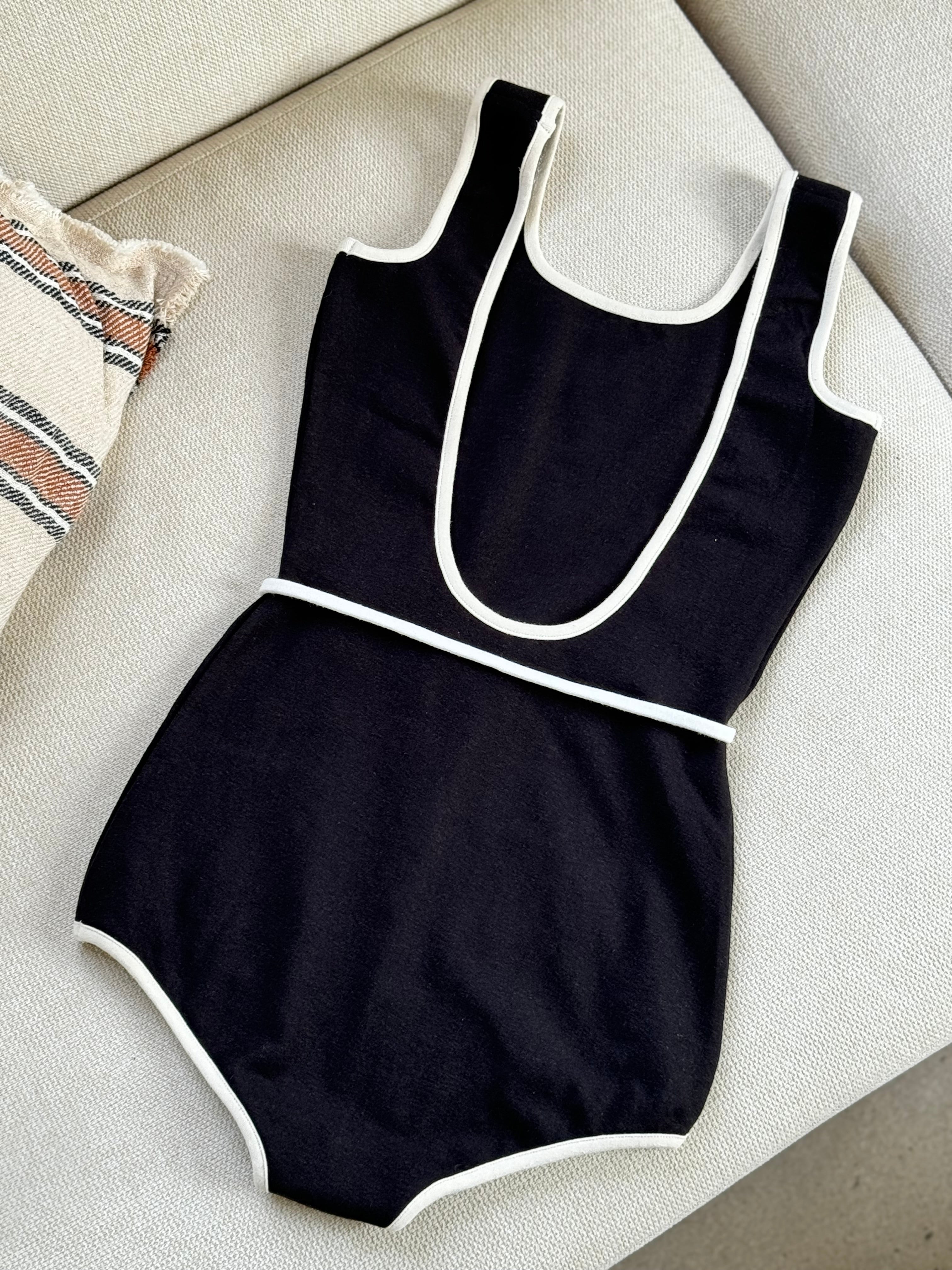 Black sustainable swimsuit with white trim on a couch surface