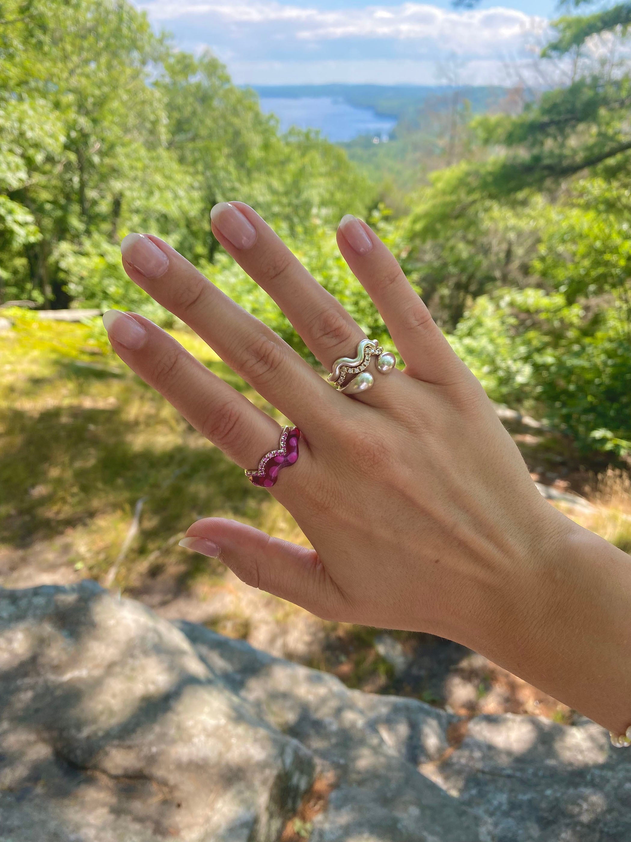 A hand model wearing the single wave silver ring in a ourdoor background. Made from 100% recycled metals
