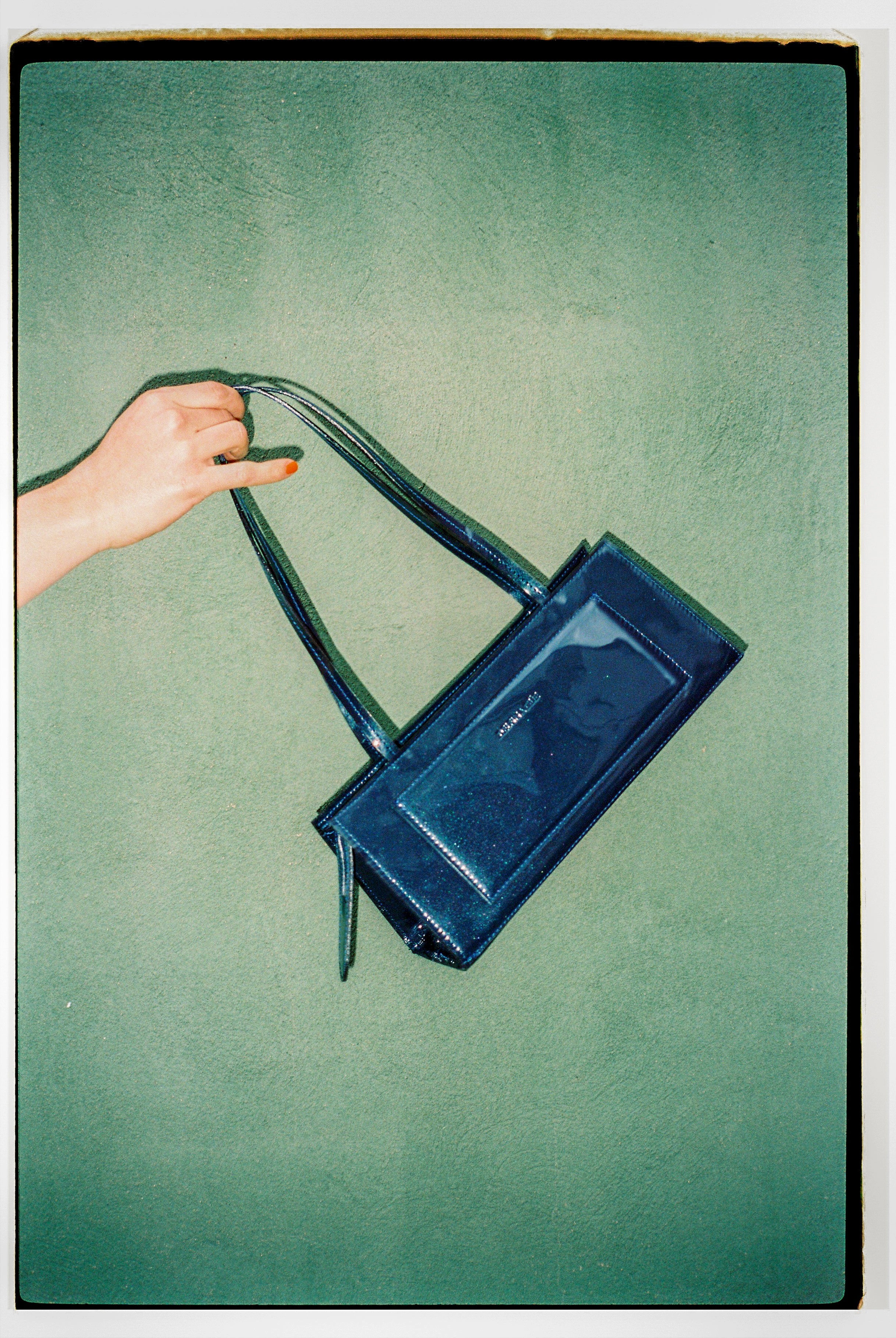 A model wearing the hotdog night blue bag in a teal background. 100% made from deadstock leather.