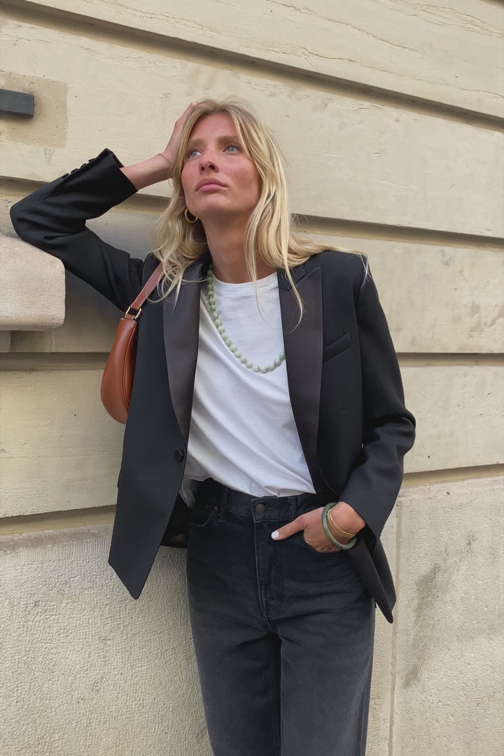 A model wearing the lauren black wool tuxedo blazer in an aesthetically outside background. 100% made from sustainable wool. 