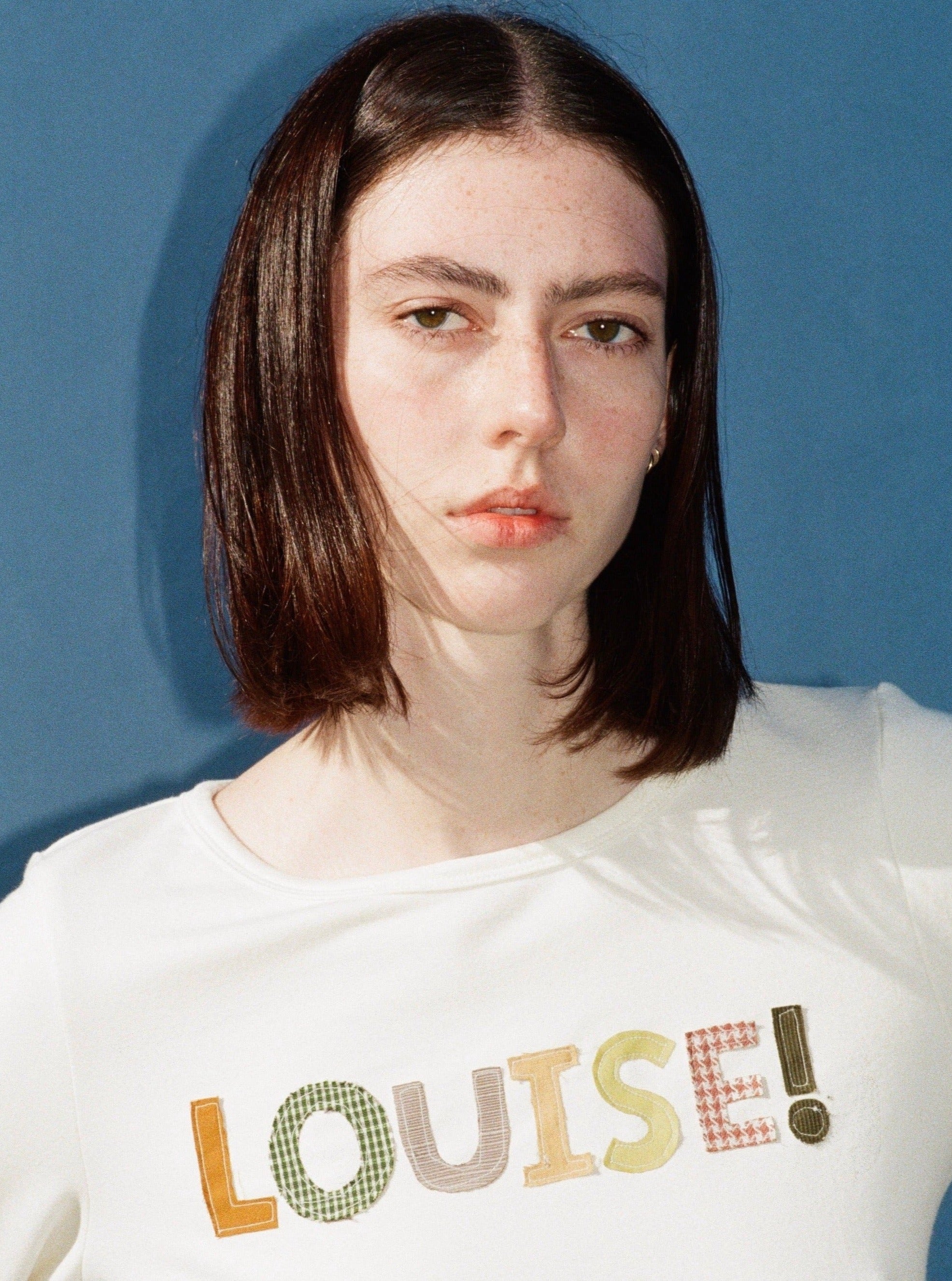 A model wearing the custom long sleeve in a blue background. Made from certified organic cotton and deadstock.